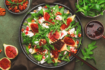 Delicious fig salad with goat cheese, nuts, arugula and jam dressing on rusty green table background, top view, copy space