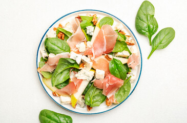 Summer pear salad with jamon, blue cheese, spinach and nuts on white table background, top view, copy space