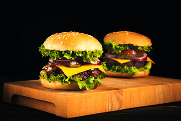 Tasty hamburgers on wooden board on dark background.
