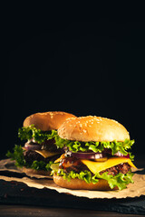 Tasty hamburgers on wooden board on dark background.