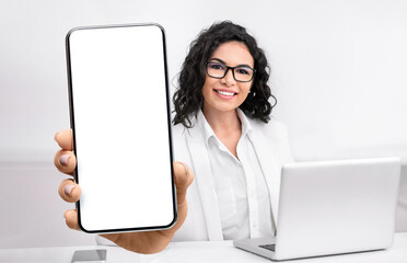 Female doctor showing big smartphone with blank screen, sitting in office at workplace, closeup, mockup
