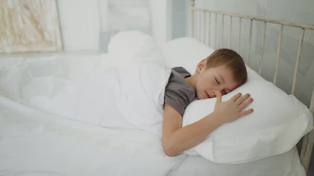 The little son sleeps in the afternoon after school on the bed. The guy sleeps in a white bed. Sleeping baby concept.