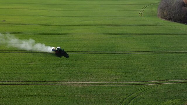 Agriculture tractor spreading fertilizer on  wheat field, aerial view
