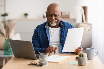 Discontented Senior Black Businessman Reading Business Papers Sitting At Workplace