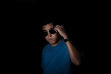 Portrait of asia man wearing sunglasses with a blue t-shirt on black background.