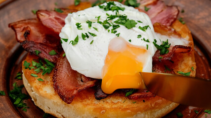 Toast with poached egg and bacon close up. Cutting poached egg with runny egg yolk over toast ....