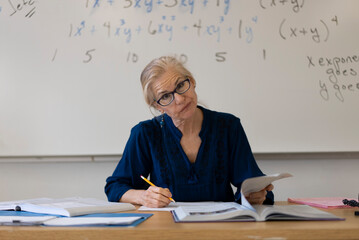 Portrait of frustrated tired high school math teacher sitting on desk talking to students.