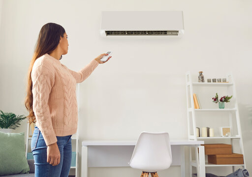 Woman turns on the AC system at home. Young girl who lives in her own house or apartment standing in the living room, holding a modern remote control and setting the temperature on the air conditioner