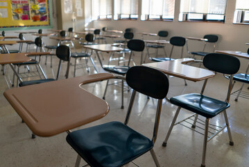 Desks in empty dark high, middle, or elementary school classroom with light coming through windows.