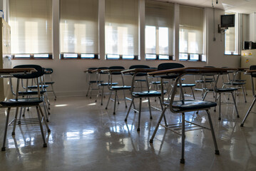 Desks in empty dark high, middle, or elementary school classroom with light coming through windows.
