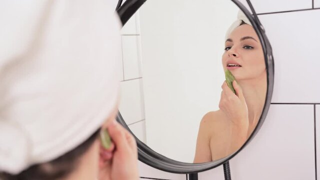 Young woman doing morning routine. Batroom maternity treatment. Health care concept. Female person. Pandemic concept. Green heart guasha acupuncture face massage