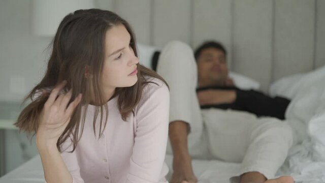 Young interracial couple relaxing on bed, woman feeling sad and bored