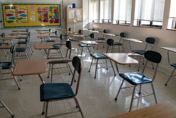 Desks in empty dark high, middle, or elementary school classroom with light coming through windows.
