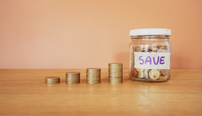 Stack of money coin and coin in a glass jar on wooden desk with brown background