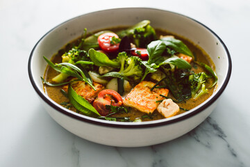 vegan thai green curry with fried silken tofu broccoli and snow peas topped with freshly picked herbs from the garden, healthy plant-based food