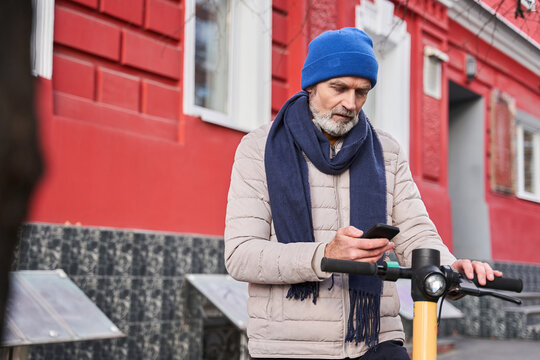 Millennial senior caucasian man using smartphone to unlocking urban kick scooter