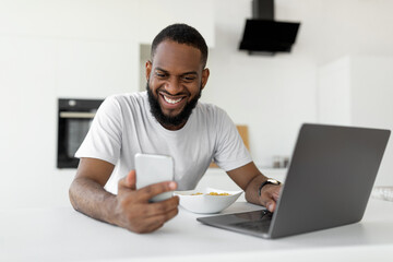 Black man using pc and smartphone having breakfast at home