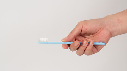 Hand holding blue toothbrush on white background.