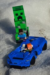 Obraz premium LEGO Minecraft Alex rescuing Steve from attack of giant green explosive Creeper mob, lifting him on board of LEGO Creator McLaren Elva light super sport car in snowy landscape.