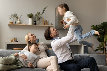 Happy laughing strong dad lifting cute little excited screaming daughter girl up in air. Cheerful...