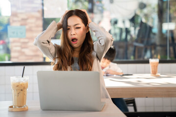 Businesswoman wearing suit and looking at laptop feeling headache sitting in the coffee shop with a cup of ice coffee. Working with notebook, freelancer, internet. Business and meeting concept