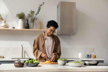 Happy pretty Black girl enjoying cooking hobby, chopping fresh vegetables for salad at kitchen...