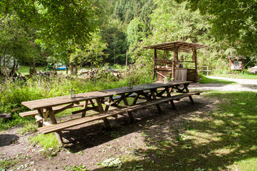 Fototapeta na wymiar Wooden tables and benches suitable for lunch or snack in the woods next to a green meadow in the camp.