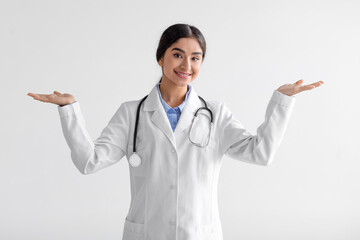 Smiling young indian female doctor show both hands open palms, presenting and advertising comparison and balance