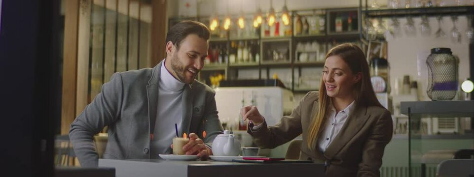 Adult Caucasian couple spending time in retro style cafe. Sitting at small table, drinking tea or coffee and speaking together.
