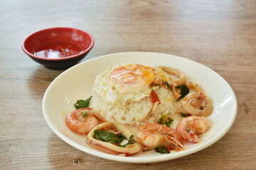 spicy stir fried shrimp and squid basil leaf topping egg eat couple with rice on plate