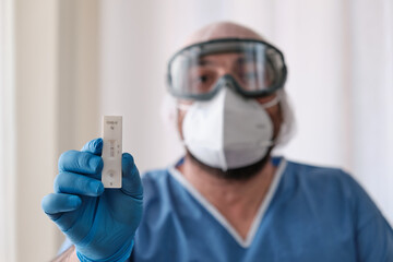 A doctor wearing latex gloves holds a covid-19 antigen test that has come back negative