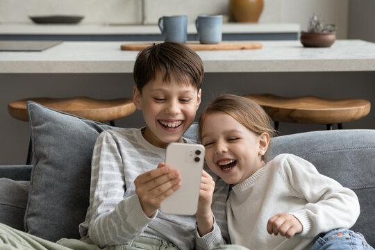 Happy cheerful gen Z sibling kids watching funny media on smartphone, making video call to parent, playing online game, virtual videogame, using learning app on internet, laughing. Parental control
