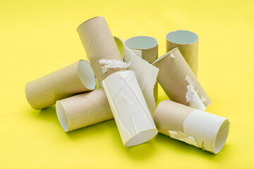 A pile of empty toilet paper tubes on a yellow background. The concept is a global crisis and a lack of things to meet basic needs.