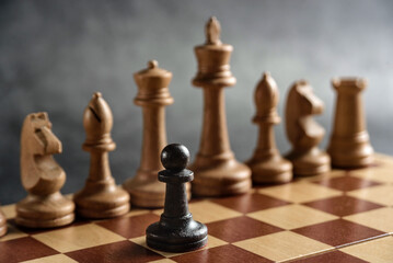 The black chess pawn opposes the white pieces. The concept of struggle, conflict, overcoming.