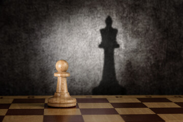 a lone pawn on a chessboard casts the queen's shadow on the wall.