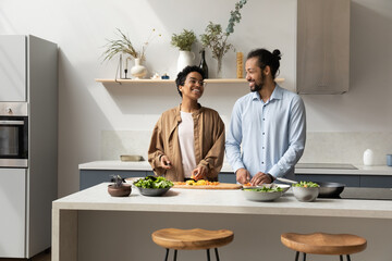 Happy millennial dating African couple preparing salad for dinner in home kitchen together, slicing fresh vegetables, cooking from organic food ingredients, talking, laughing, keeping healthy eating