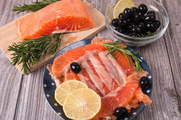 Slicing red fish on a plate with olives lemon and rosemary