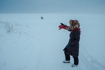 A girl wearing a Russian folk shawl stands on the shore of the White Sea in winter