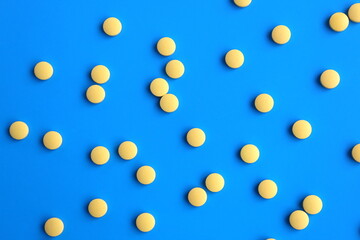 The texture of many yellow pills lie on a white background.