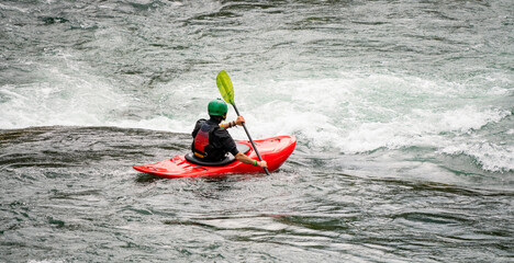 River kayaker in red kayak are paddling whitewatered river. Extreme sports and adrenaline concept. Removed logos.