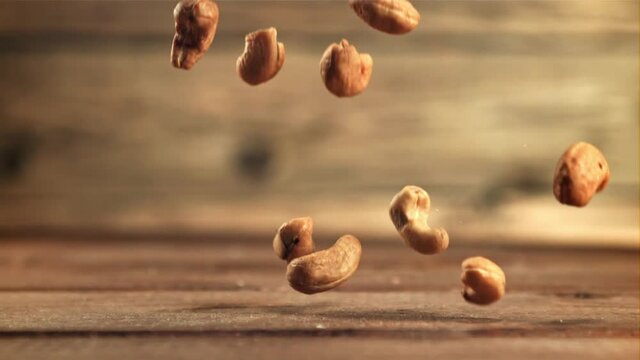 Cashew nuts fall on the table. On a wooden background. Filmed is slow motion 1000 frames per second. High quality FullHD footage