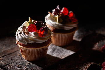 Two cupcakes decorated with berries on a dark background