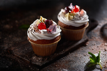 Two cupcakes decorated with berries on a dark background