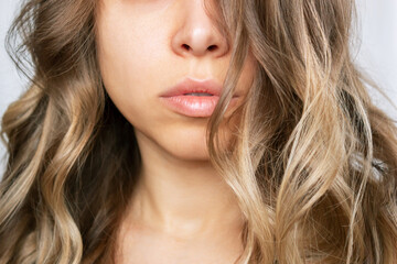 Cropped shot of a young caucasian blonde woman with wavy hair isolated on a white background. Result of coloring, highlighting, perming. Beauty and fashion. Lower part of the face. Hair styling