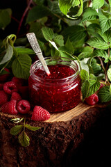 Jar of raspberry jam and fresh berries with leaves.
