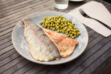 Top view of baked trout fillet served on plate with peas closeup