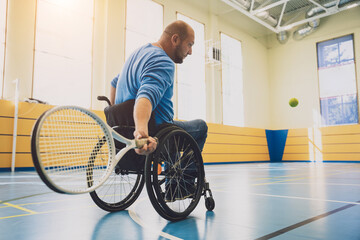 Adult man with a physical disability who uses wheelchair playing tennis on indoor tennis court - obrazy, fototapety, plakaty