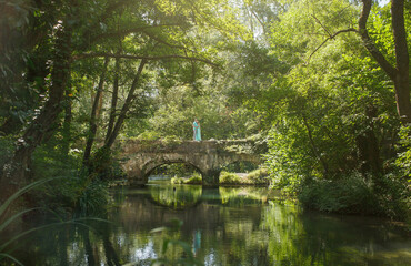 a guy and a girl are standing on a bridge over a river in the forest. Green clothes.