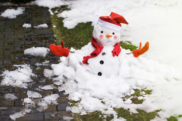 Unhappy snowman in mittens, red scarf and cap is melting  outdoors in sunlight on snowy background...