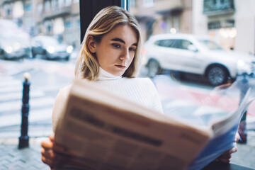 Serious female reading newspaper in cafeteria